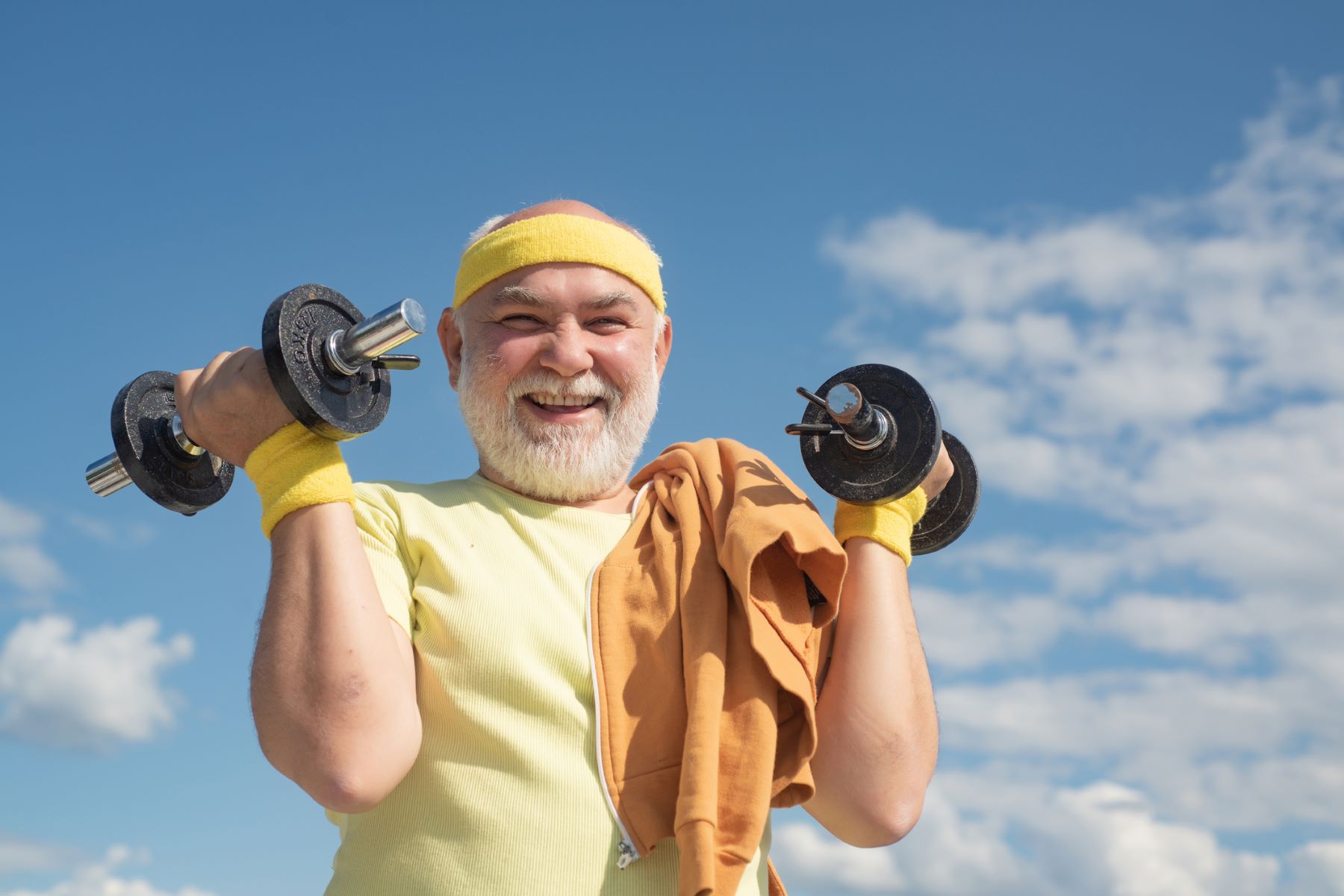Smiling senior man exercising outside with dumbbells