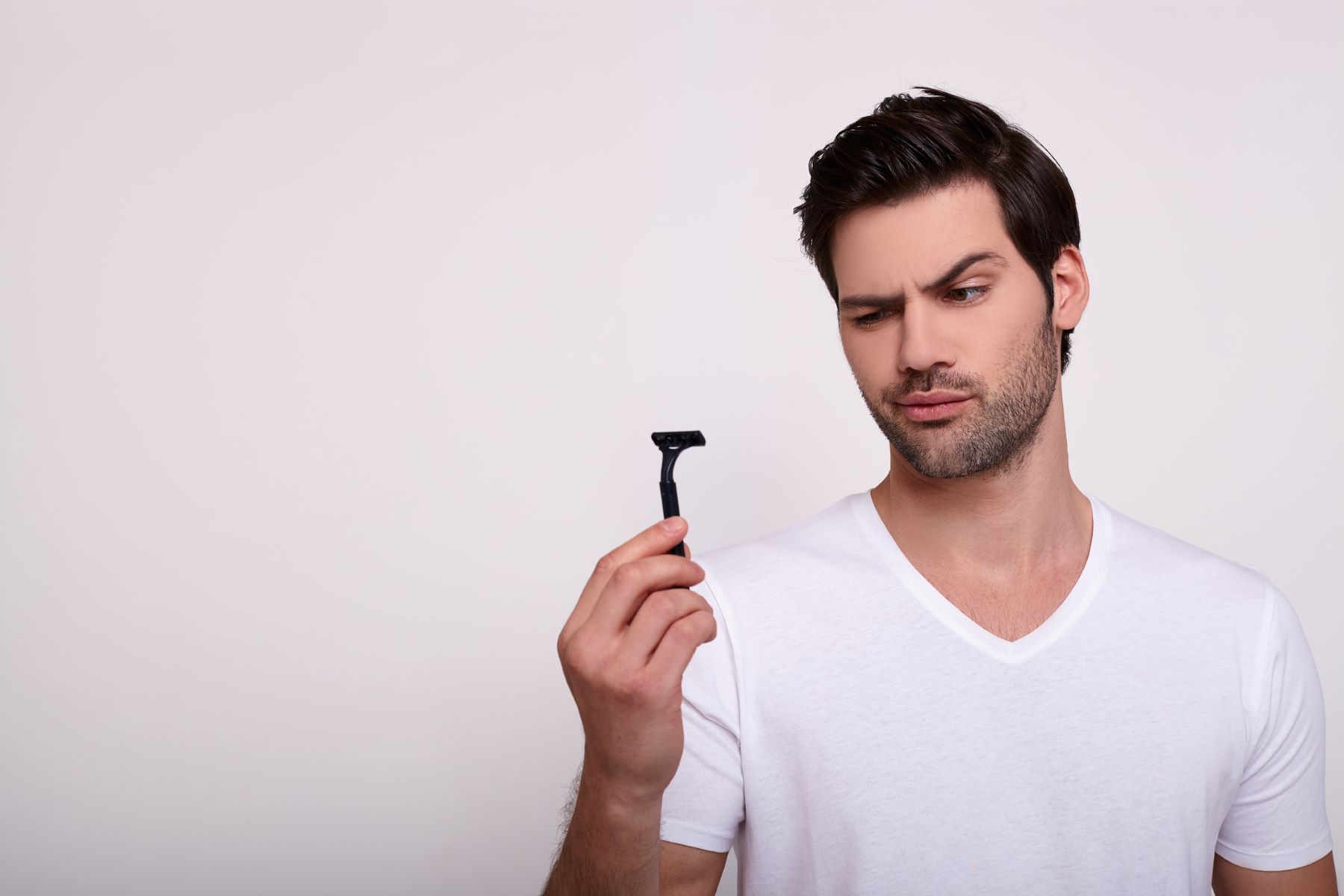 Young man holding a razor and looking skeptically at it