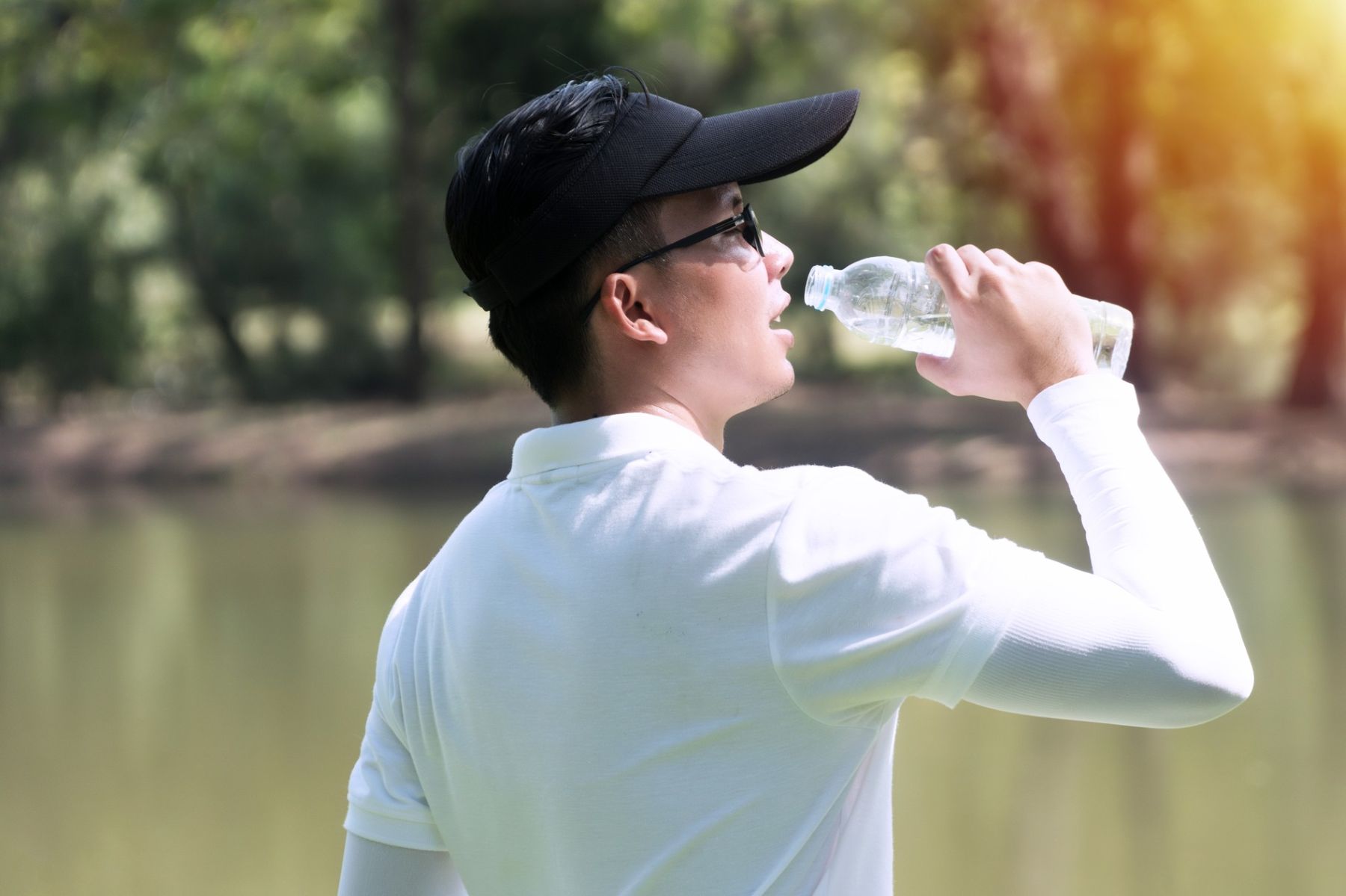 Man wearing a hat and drinking water to prevent dry hair